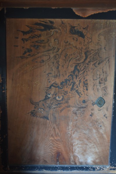 A well-worn door in the the sake-making building with a simple painting of a dragon